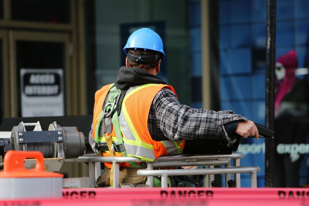 Worker with hardhat, orange reflective vest, and safety harness behind DANGER tape