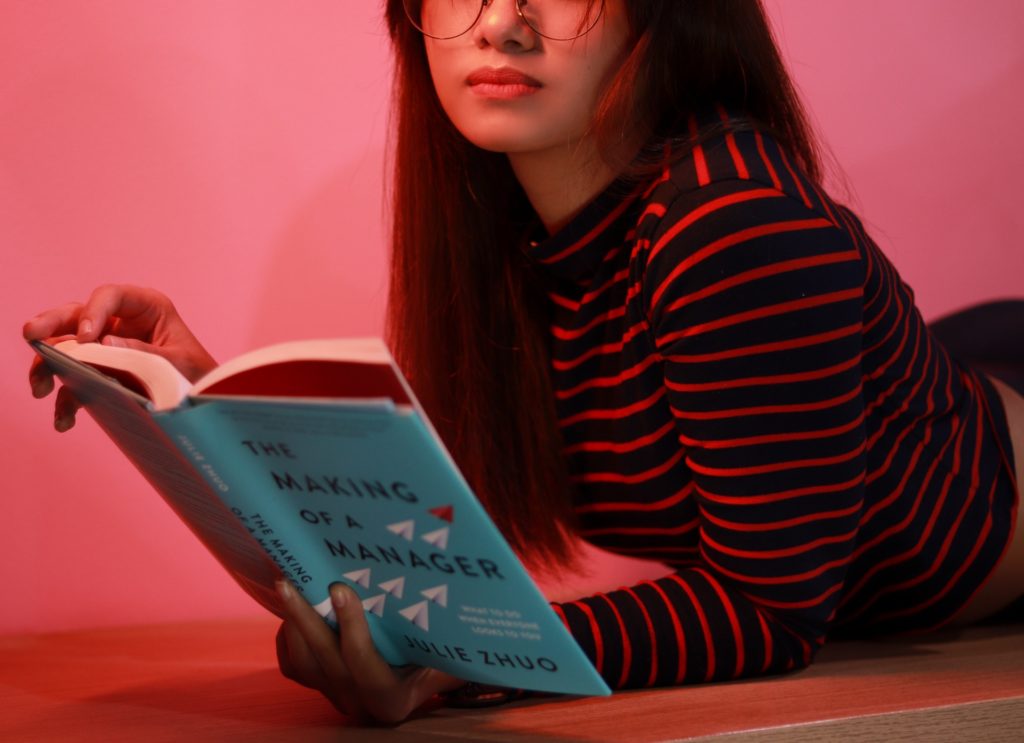 Woman wearing glasses reading a book titled The Making of a Manager