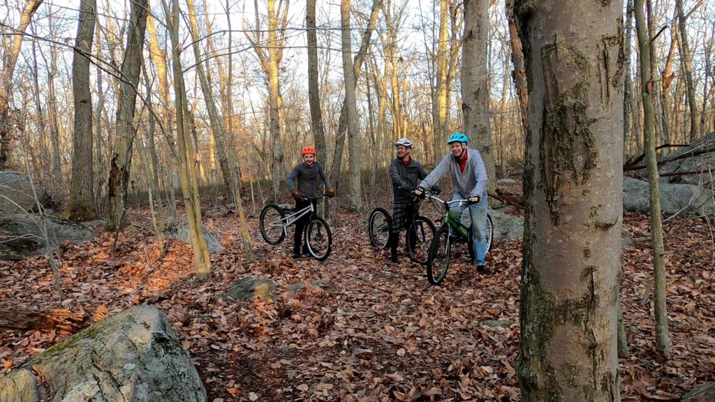 Three trials bike riders in the woods with their bikes, laughing